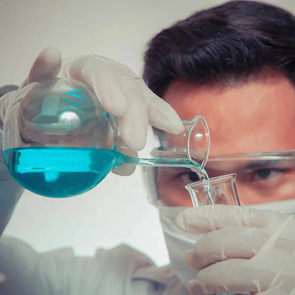 Imagem mostra um homem branco de óculos e mascara manuseando produtos dentro de uma laboratório